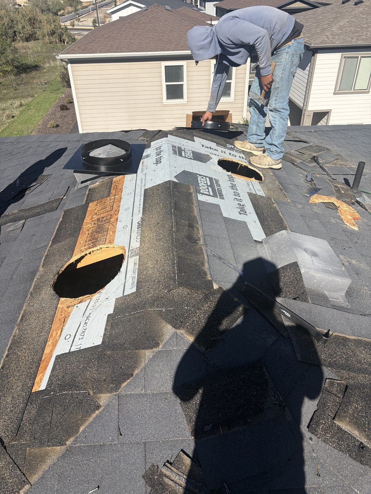 Ridge repair with underlayment opened along the ridge, vent holes cut, and a worker fitting the new ridge.