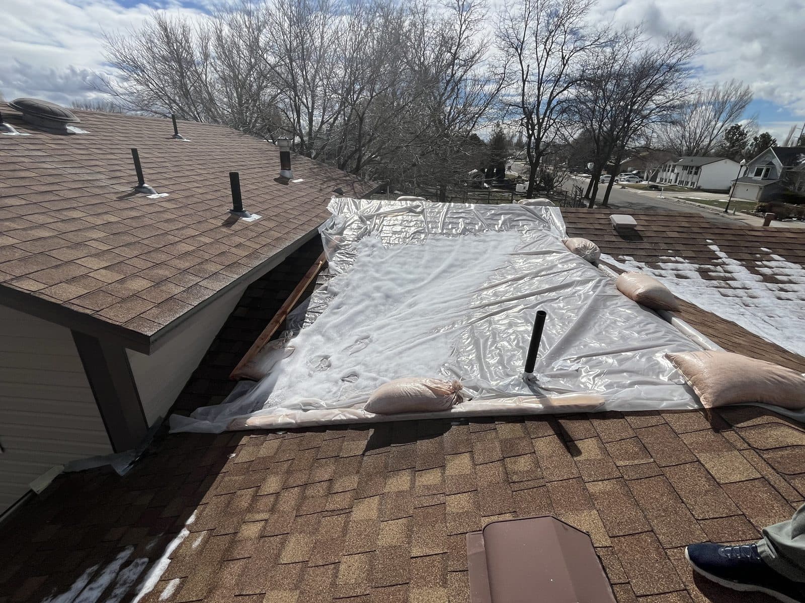 Large plastic emergency cover weighted with sandbags over a section of roof.