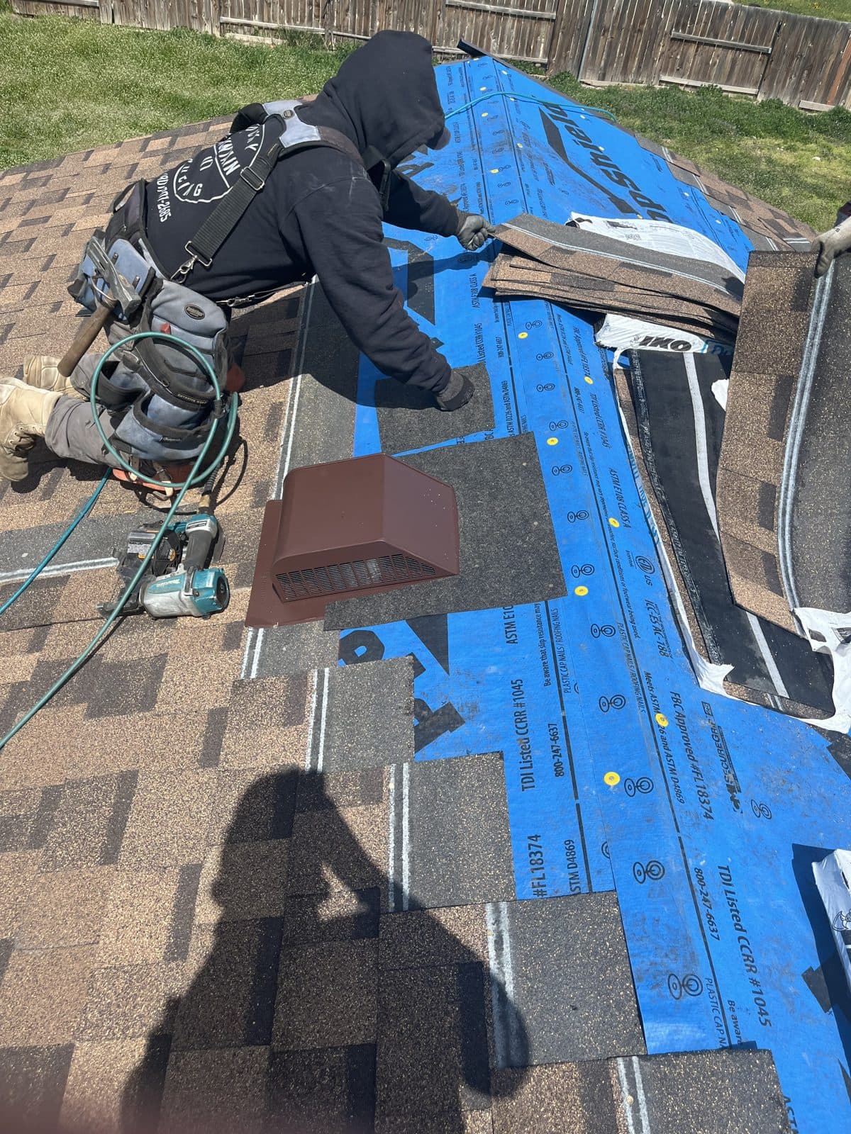 Installer setting architectural shingles over synthetic underlayment around a plumbing vent.