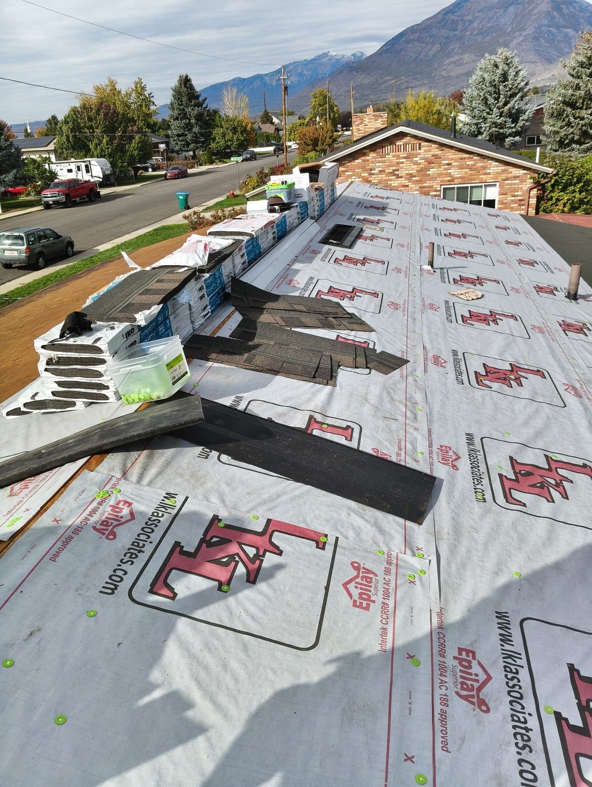 Underlayment installed and bundles of architectural shingles staged on the roof, with a mountain neighborhood beyond.