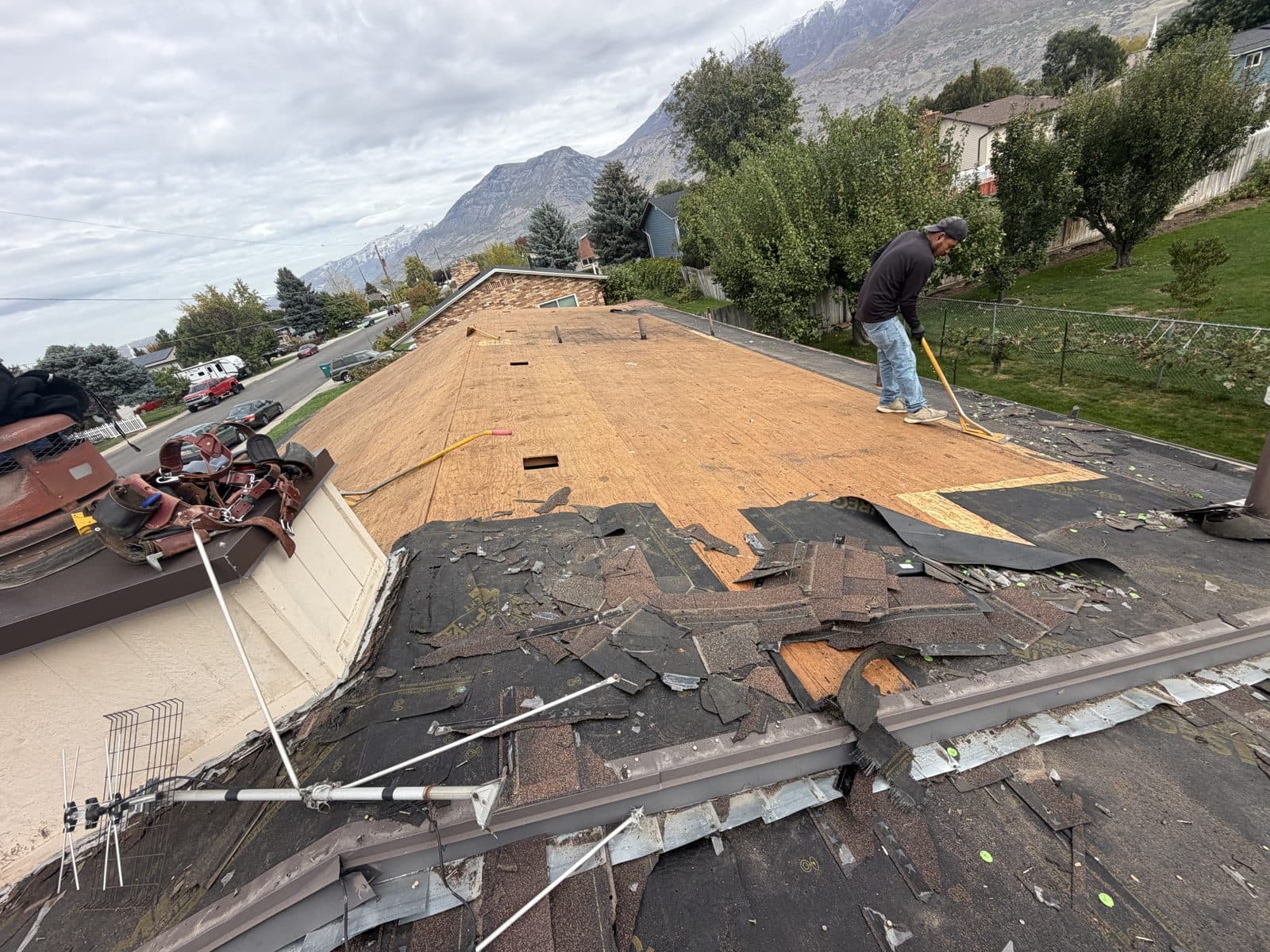 Crew tearing old asphalt shingles off a roof down to the decking, with mountains in the background.